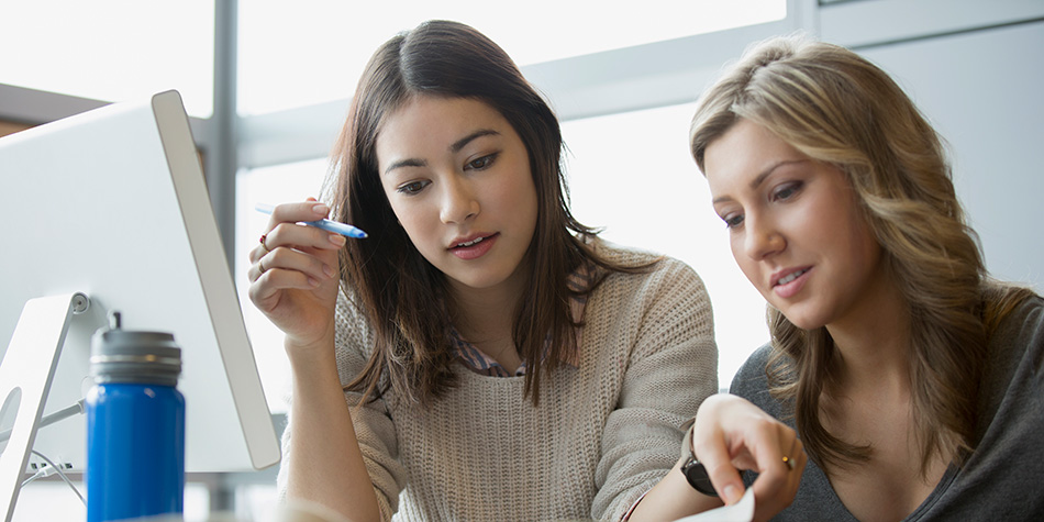 Two young women sitting at a desk reviewing a book